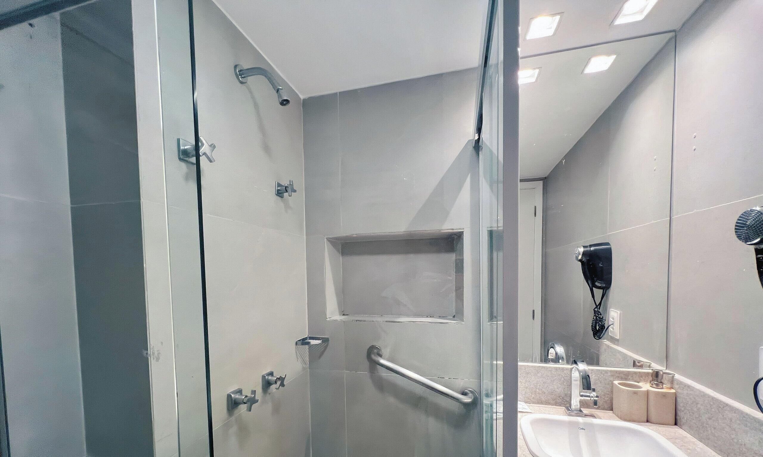 A modern bathroom with a glass-enclosed shower, a sink, a hairdryer, and a mirror.
