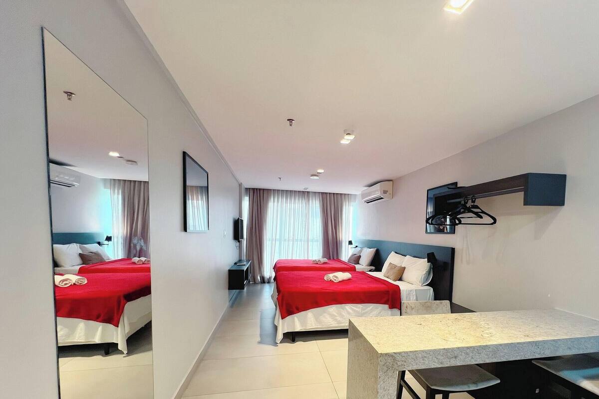 A hotel room with two beds, a desk, a chair, a TV, and an air conditioning unit.