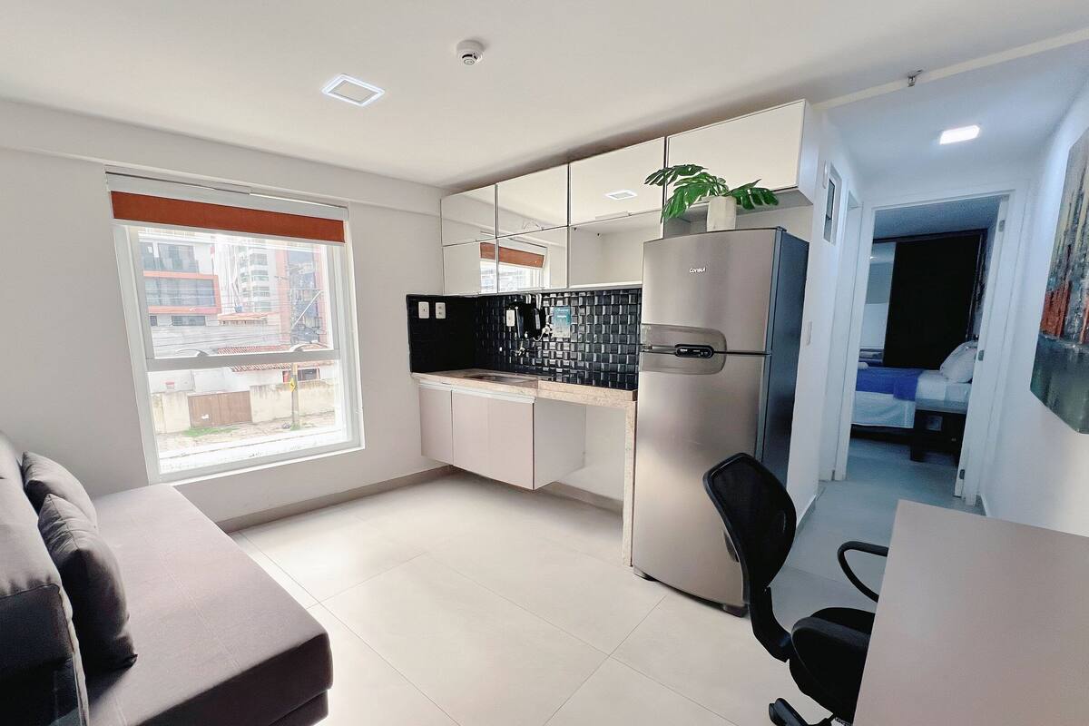 A modern kitchen with a refrigerator, a countertop, and a window with blinds.