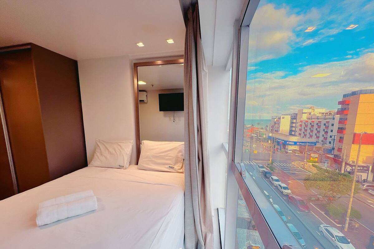 A hotel room with a bed, a window with a city view, and a television on the wall.