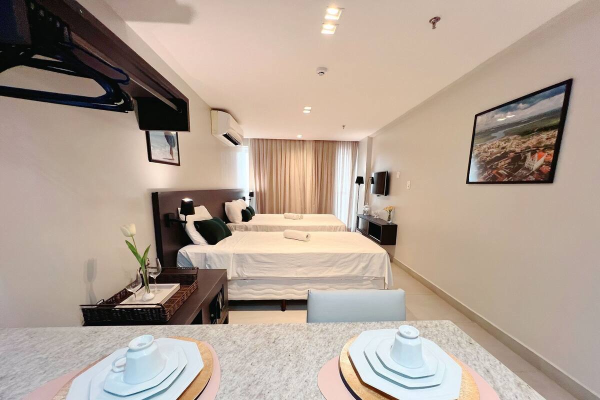 A hotel room with two beds, a dining table with plates, a TV, and a painting on the wall.