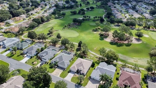 An aerial view of a residential area with houses, a golf course, and a large body of water in the distance. - Golf View in the Villages (The Villages)
