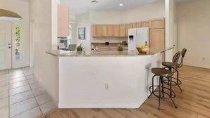 A modern kitchen with a central island, wooden cabinets, and a bar area with stools. - Golf View in the Villages (The Villages)