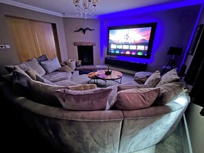 A modern living room with a curved sectional sofa, a coffee table, a flat-screen TV, and ambient lighting.