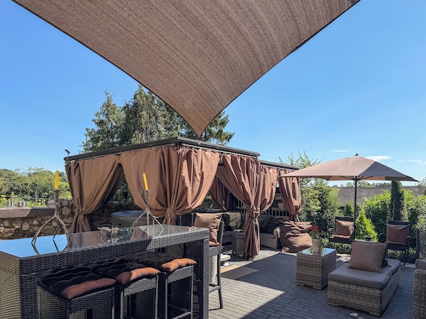 An outdoor patio area with wicker furniture, a covered seating area, and a view of the surrounding greenery.