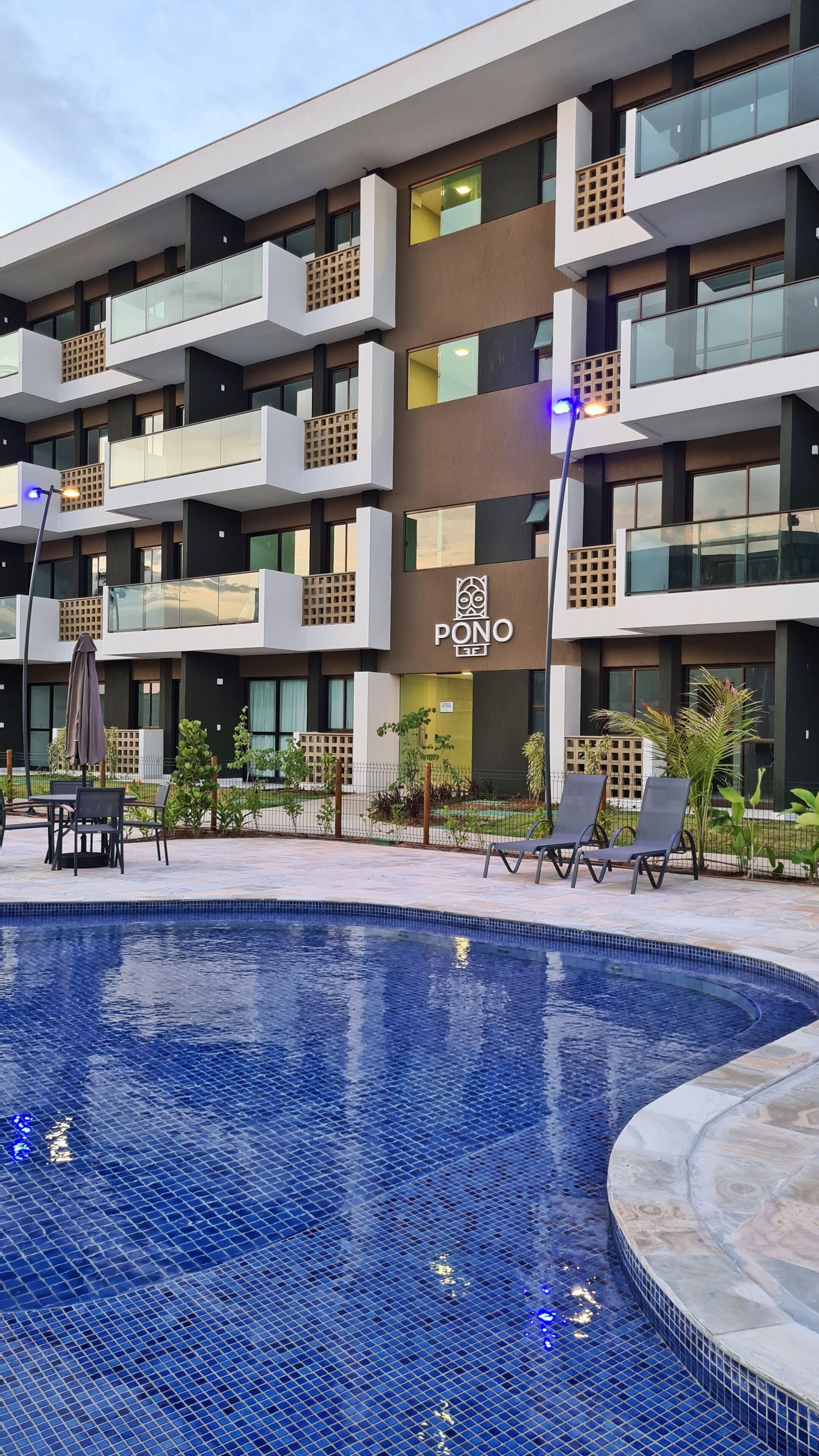 Un hotel moderno con área de piscina, mobiliario exterior y un letrero que dice "PONO".