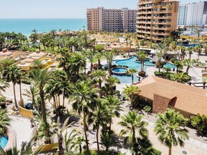 A resort with multiple swimming pools, palm trees, and a view of the ocean.