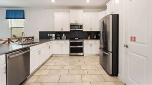 Una cocina moderna con armarios blancos, electrodomésticos de acero inoxidable y piso de baldosas.