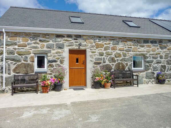 A stone building with a wooden door, two windows, and a bench outside.