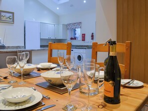 A dining table set with wine glasses, plates, and a bottle of wine in a room with a washing machine and cabinets in the background.