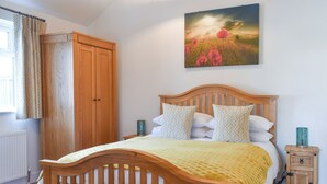 A bedroom with a wooden bed, a wooden nightstand, a wooden bench, a wardrobe, and a painting of a field.