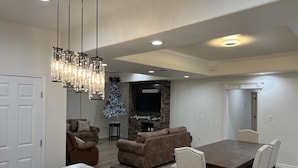 A dining area with a marble table, wooden chairs, and a chandelier. There is a fireplace with a stone surround and a television mounted on the wall. - Casa Recuerdos (Del Rio)