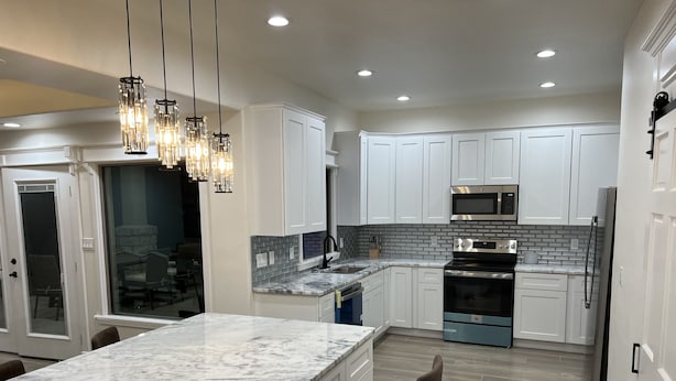 A modern kitchen with white cabinets, a marble island, stainless steel appliances, and pendant lighting. - Casa Recuerdos (Del Rio)