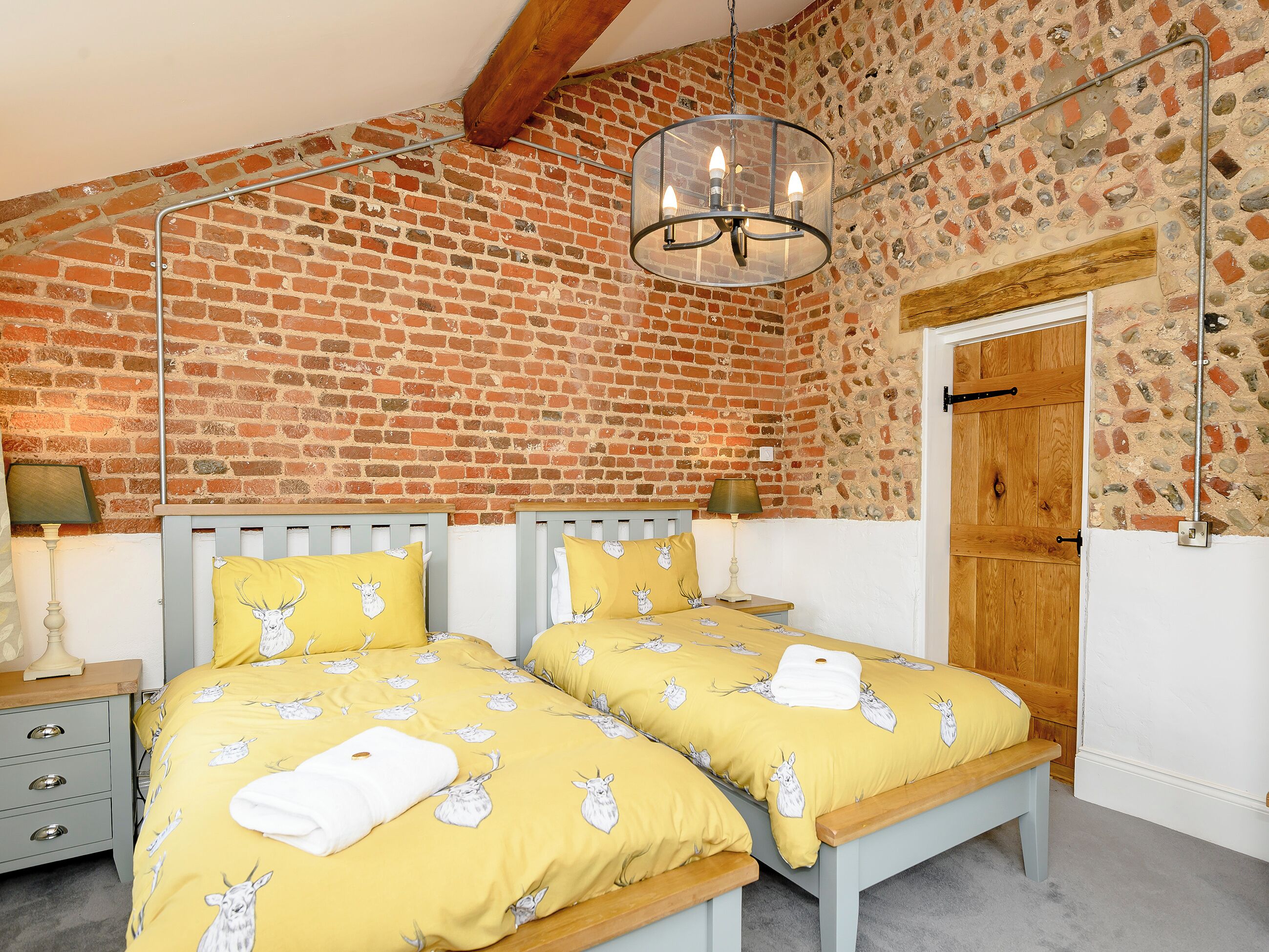 A bedroom with two beds, a brick wall, a wooden door, and a hanging light fixture.
