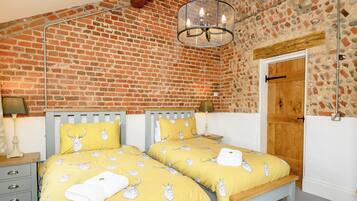 A bedroom with two beds, a brick wall, a wooden door, and a hanging light fixture.