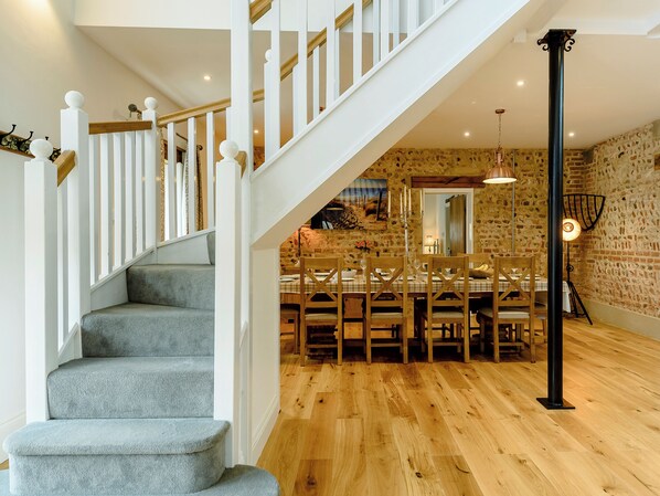 A staircase with white railings and grey carpet leading to a dining area with wooden chairs and a table.