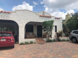 Une maison à l’extérieur blanc, avec deux portes de garage apparentes, une voiture rouge garée devant et une allée pavée.