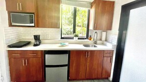 A compact kitchen with wooden cabinets, a built-in microwave, a coffee maker, and a dishwasher. - Studio in Little Havana - Free Gated Parking (Miami)