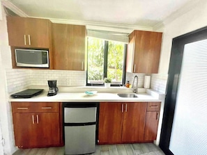 A compact kitchen with wooden cabinets, a built-in microwave, a coffee maker, and a dishwasher.