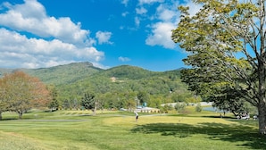 Un campo de golf con cielo despejado, árboles y una montaña al fondo.