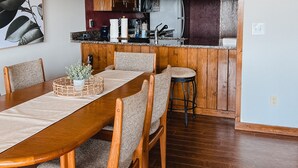 Un comedor con una mesa y sillas de madera, una cocina al fondo y un reloj en la pared.