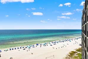 A beach with clear blue water, umbrellas, and people.