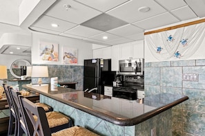 A modern kitchen with a central island, stainless steel appliances, and a backsplash with a blue and green pattern. - Turtle Nest- Edgewater T3-Beachfront-1 BD/1BTH-Sleeps 4-Mesmerizing Views! (Panama City Beach)