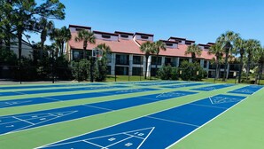 Ein Shuffleboard-Spielfeld mit nummerierten Zählfeldern und ein Gebäude mit roten Ziegeldächern im Hintergrund.