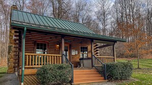 A log cabin with a porch, a hot tub, and a staircase leading to the entrance.
