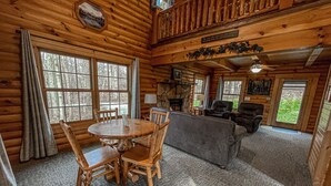 A log cabin interior with a dining table, chairs, a sofa, and a fireplace.