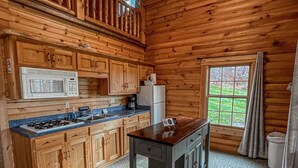 A wooden cabin interior with a kitchen featuring a stove, microwave, and refrigerator.