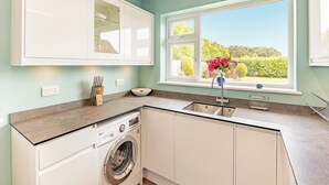 Una cocina moderna con lavadora integrada, una ventana con vistas a zonas verdes y una encimera con fregadero.