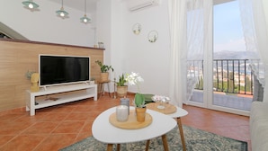 Ein modernes Wohnzimmer mit Flachbildfernseher, Holzboden, einem Balkon mit Blick und dekorativer Wandkunst.
