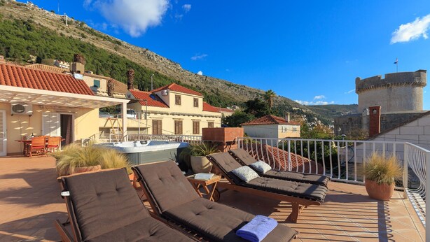 A terrace with sun loungers, a pool, and a view of a hill and castle.