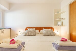 A hotel room with a double bed, two pillows, a nightstand with a lamp, a wooden wardrobe, and a shelf with decorative items.