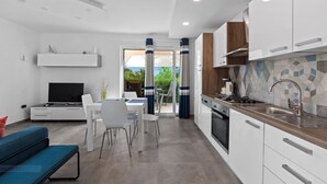 A modern kitchen with white cabinets, a tiled backsplash, and a built-in oven. There is a dining area with a table and chairs, and a TV on a stand. - Villa Vintiana - Private Pool, Six Bedrooms (Vintijan)