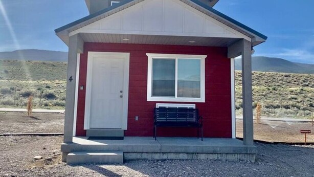 A small red building with a white door and window, a bench outside, and a clear sky. - Home Base Resort  #4 (Joseph)