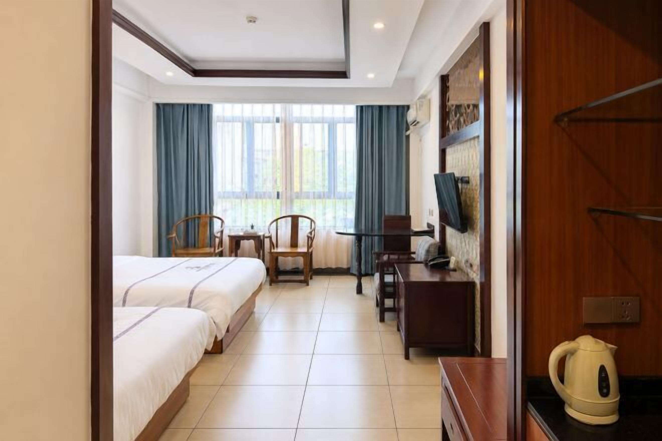 A hotel room with two beds, a desk, a chair, a television, and a window with curtains.