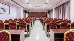 A conference room with rows of tables and chairs, a projector screen, and a stage. - Jingshan Hotel (Haikou)