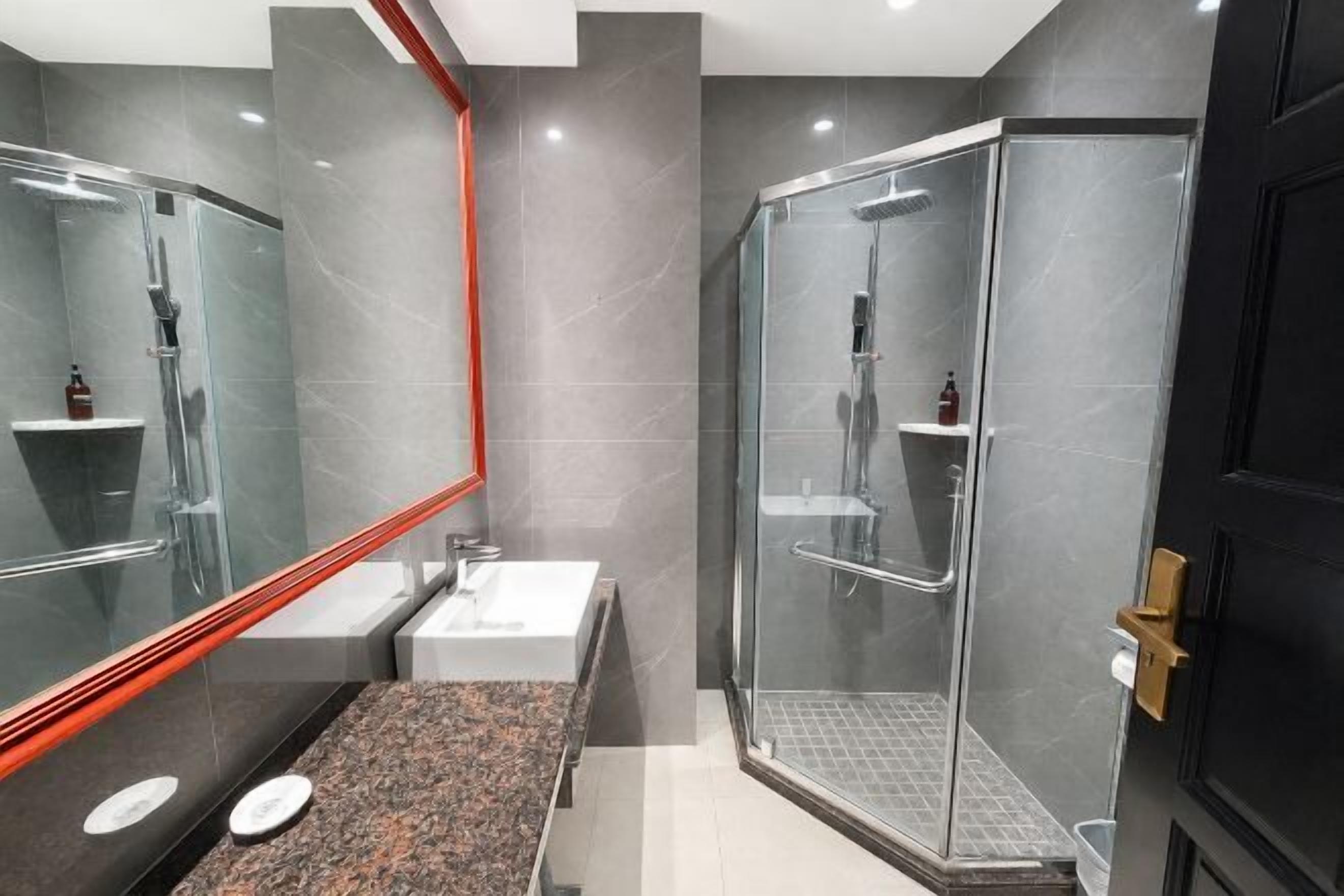 A modern bathroom with a glass shower enclosure, a large mirror, and a granite countertop.
