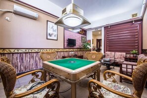 A room with a pool table, wicker chairs, a television, and a large window with blinds. - Jingshan Hotel (Haikou)