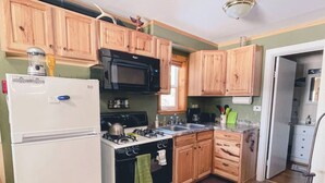 Una cocina con armarios de madera, un refrigerador blanco, un microondas negro, una estufa y un lavamanos.