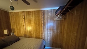 Un dormitorio con paneles de madera, una cama con cubierta acolchada, una lámpara de noche y un ventilador de techo.