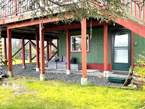 A covered porch with a seating area, a green door, and a small garden.