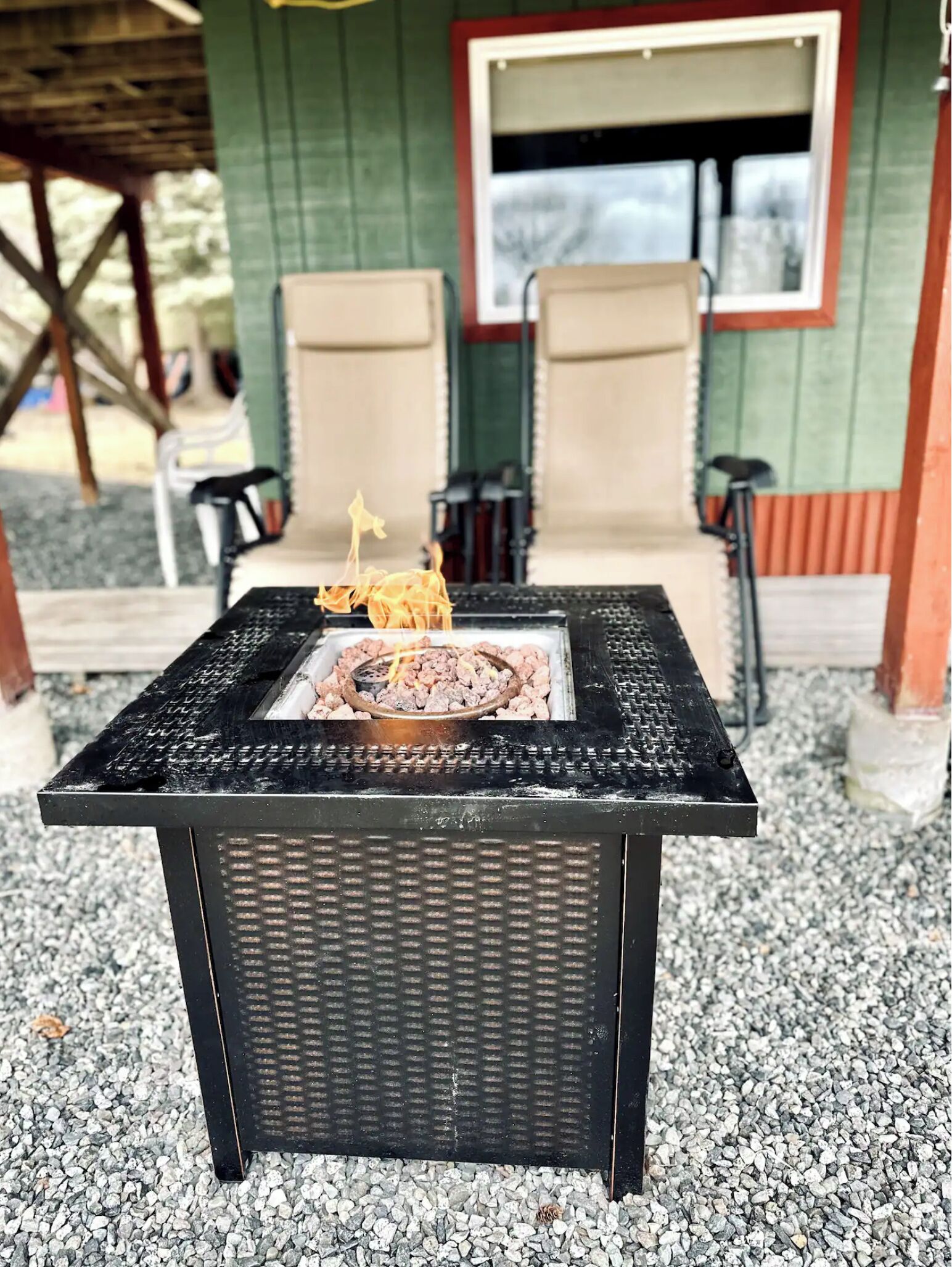 Ein schwarzes Grilltablett im Freien, mit Feuer und umgeben von Kies.