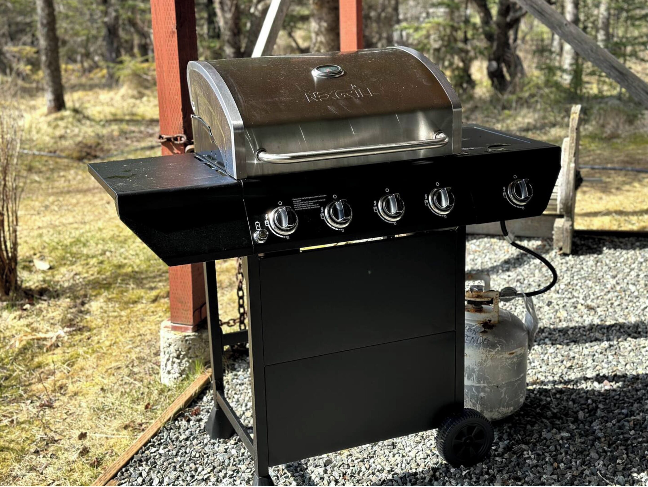 Un barbecue au gaz portatif doté de quatre brûleurs, d’une étagère latérale et d’une bouteille de gaz.