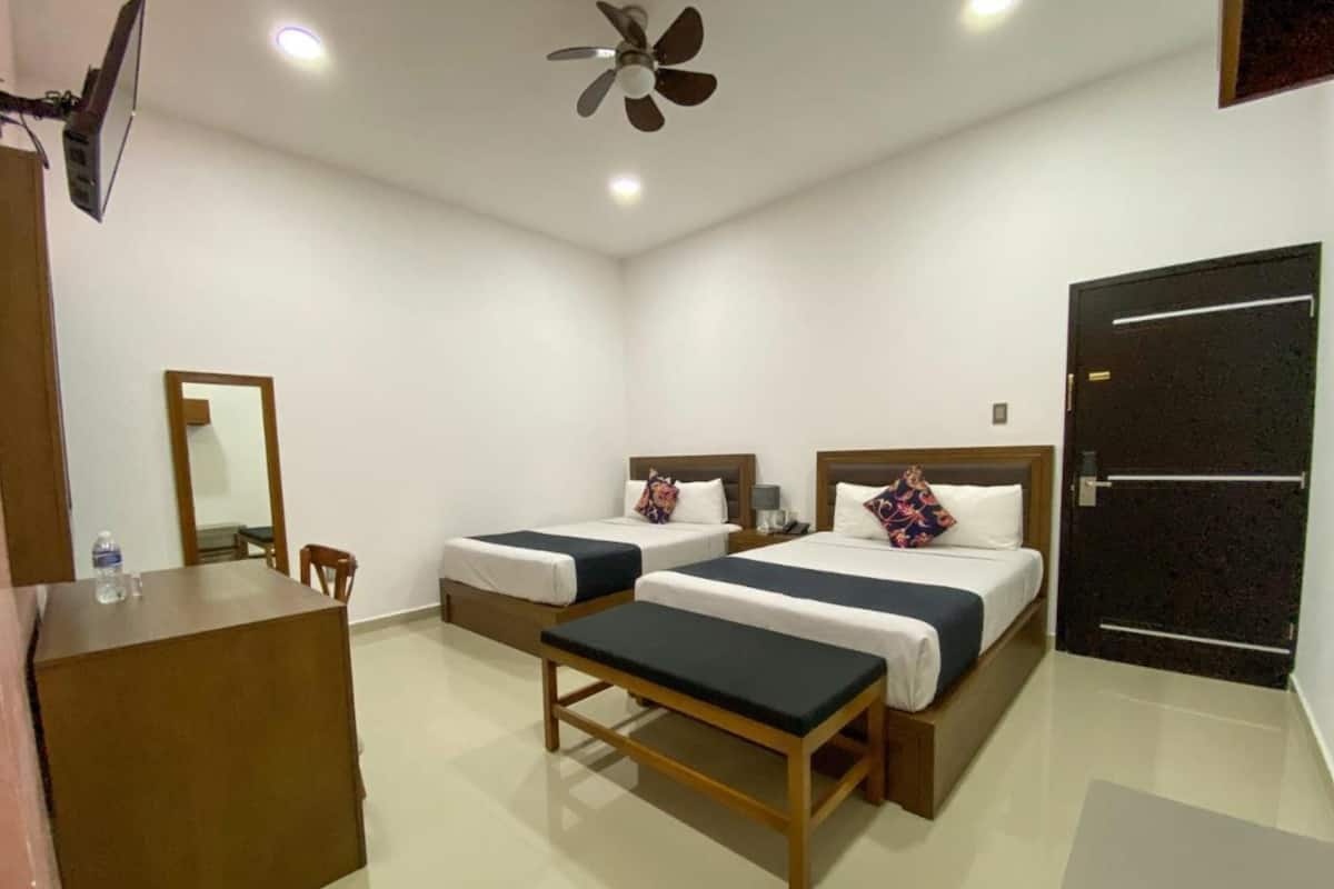 A hotel room with two beds, a desk, a chair, a mirror, a ceiling fan, and a door.