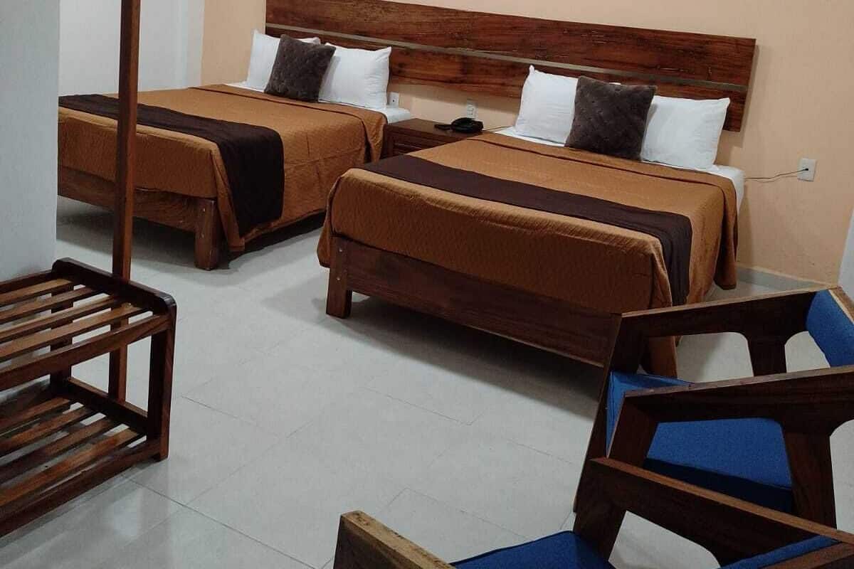A hotel room with two beds, a wooden headboard, a ceiling fan, and a wooden chair with a blue cushion.