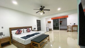 Una camera d'albergo moderna con un letto grande, comodini, una panca, una ventola a soffitto e una porta scorrevole che dà su un balcone.