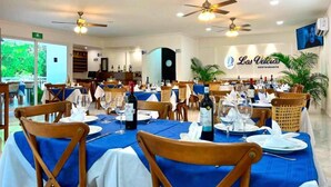 Un ristorante con diversi tavoli apparecchiati, ventilatori a soffitto e vista sull'esterno.